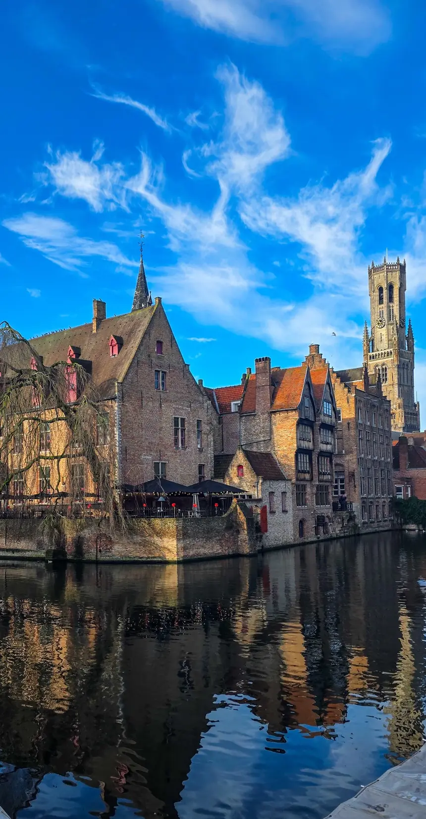 El Rozenhoedkaai de Brujas reflejado en el canal, con el campanario al fondo